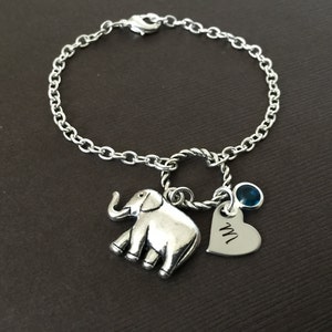 Puede incluir: Un brazalete de cadena de plata con un dije de elefante de plata, un dije de coraz&oacute;n de plata con la letra "M" grabada y un dije de piedra preciosa azul.