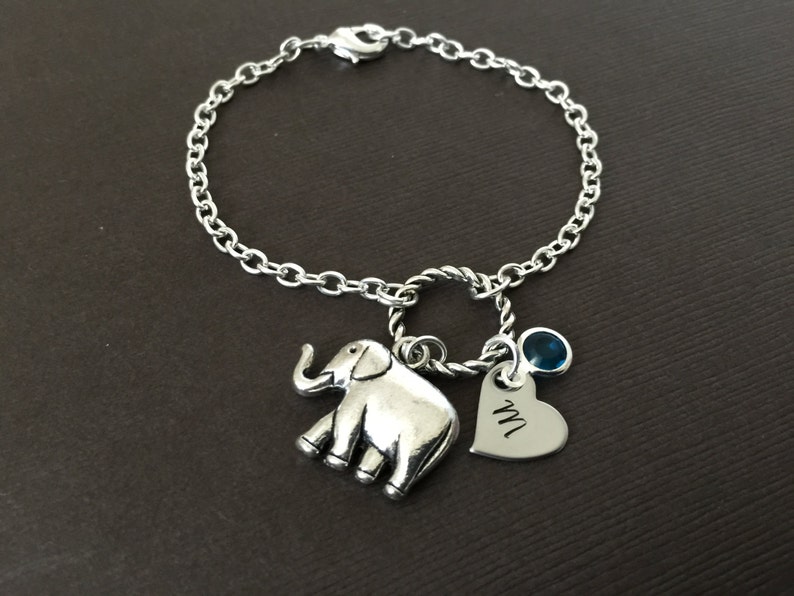 Puede incluir: Un brazalete de cadena de plata con un dije de elefante de plata, un dije de coraz&oacute;n de plata con la letra "M" grabada y un dije de piedra preciosa azul.