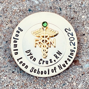 Peut inclure: &Eacute;pinglette ronde dor&eacute;e avec un bijou vert et un symbole de caduc&eacute;e. Le texte sur l'&eacute;pingle est "Benjamin Leon School of Nursing, Dylan Cruz, RN, 2022".