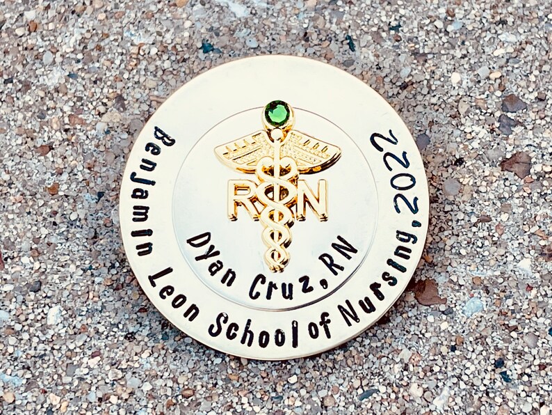 Peut inclure: &Eacute;pinglette ronde dor&eacute;e avec un bijou vert et un symbole de caduc&eacute;e. Le texte sur l'&eacute;pingle est "Benjamin Leon School of Nursing, Dylan Cruz, RN, 2022".