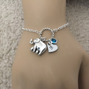Puede incluir: Pulsera de plata con un dije de elefante, un dije de coraz&oacute;n con la letra "M" grabada y un dije de piedra azul.