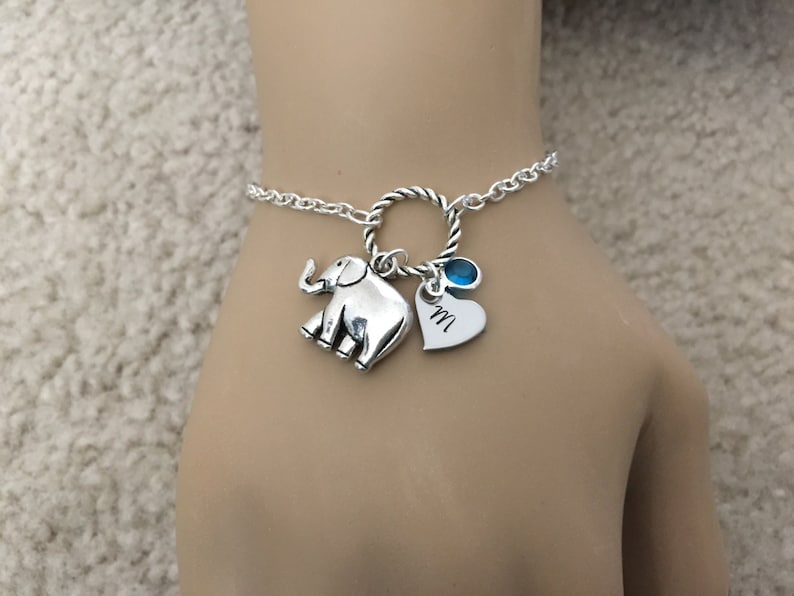 Puede incluir: Pulsera de plata con un dije de elefante, un dije de coraz&oacute;n con la letra "M" grabada y un dije de piedra azul.