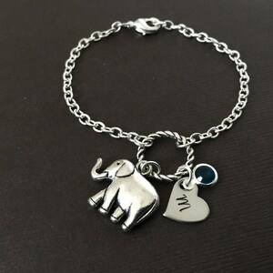 Puede incluir: Un brazalete de plata con un dije de elefante, un dije de coraz&oacute;n con la letra "M" grabada y un dije de piedra preciosa azul.