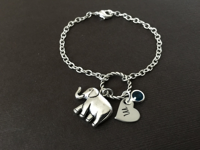 Puede incluir: Un brazalete de plata con un dije de elefante, un dije de coraz&oacute;n con la letra "M" grabada y un dije de piedra preciosa azul.
