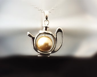 May include: A silver teapot pendant necklace with a pearl inside. The pearl is a light gold color.