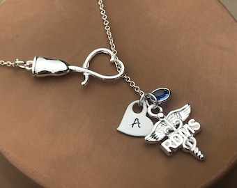 May include: Silver necklace with a stethoscope charm, a heart charm with the letter A, a caduceus charm with the word "RN" and a blue crystal charm.