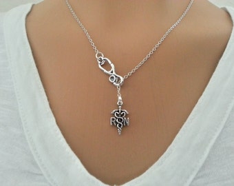 May include: A silver necklace with a stethoscope charm and a pendant with a caduceus and the letters "RN".