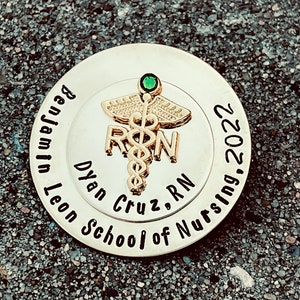 Peut inclure: &Eacute;pinglette ronde dor&eacute;e avec un bijou vert et le texte "Benjamin Leon School of Nursing, 2022" et "Dylan Cruz, RN" avec un symbole de caduc&eacute;e.