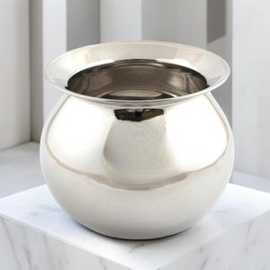 May include: A polished silver metal pot with a spherical body and a flared rim. The pot is displayed on a white marble surface. The design is simple and elegant, suitable for various uses. The pot's dimensions are approximately 15 cm in diameter.