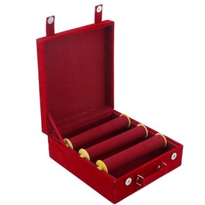 May include: A red velvet jewelry box with three cylindrical holders. The box is open, revealing the interior. The holders have yellow accents. The box has a handle and two clasps.