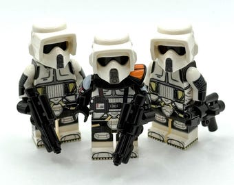 May include: Three plastic scout trooper minifigures with white helmets and armour featuring black detailing. Each figure holds a black plastic blaster accessory. The central figure displays an orange shoulder pauldron and unique chest markings.