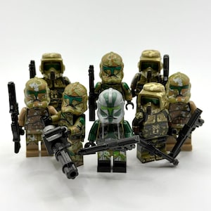 Könnte beinhalten: Eine Sammlung von sieben Kunststoff-Spielzeugsoldaten-Minifiguren mit Tarnmuster-Rüstung in Beige-, Braun- und Grüntönen. Jede Figur trägt einen eigenen Helm und ein schwarzes Kunststoff-Blaster-Zubehör, wobei eine Figur in der Mitte einen weiß-grünen Helm trägt.