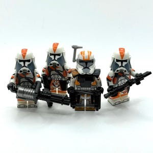 Könnte beinhalten: Vier Spielzeugsoldaten-Minifiguren aus Kunststoff mit weiß-oranger Rüstung und schwarzen Details. Jede Figur trägt einen passenden Helm mit einem orangefarbenen Streifen. Sie sind mit verschiedenen schwarzen Blastern und Waffen ausgestattet.