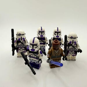 May include: Six Lego Star Wars minifigures. Five white and purple clone troopers with black weapons and one brown-skinned Jedi with a blue lightsaber. The figures are on a white background.