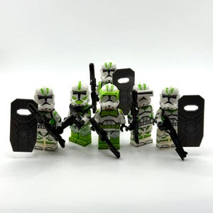 May include: A group of six white and lime green plastic toy soldier minifigures. Each figure wears a helmet with green markings and armour with green accents. They are equipped with black plastic blasters and dark grey rectangular riot shields.