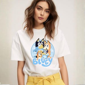 May include: White t-shirt featuring a cartoon graphic of the Bluey family in a blue circle with the word "Bluey" in light blue. The shirt is made of a soft material.