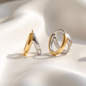May include: A pair of small hoop earrings featuring a two-tone design. Each earring is constructed with one half in a polished gold-tone finish and the other half in a polished silver-tone finish, creating a smooth, rounded, and continuous circular shape.