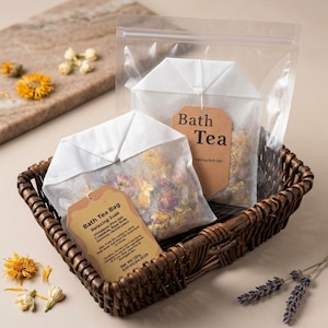 May include: A wicker basket contains two white tea bags filled with dried flowers and herbs. One bag has a brown tag that reads "Bath Tea Bag Relaxing Soak". The other bag has a tag that reads "Bath Tea". The bags are in a clear plastic bag.