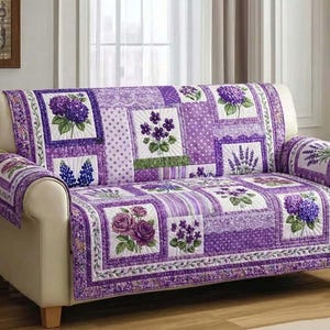 May include: A quilted sofa cover in shades of purple and white, featuring floral patchwork squares. The design includes images of hydrangeas, roses, and lavender. The cover is placed on a cream-colored sofa, with matching armrest covers.