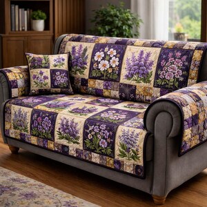 May include: A grey sofa with a floral quilt cover and matching cushion. The quilt features a patchwork design with squares of lavender, white daisies, and other purple and green floral patterns. The sofa has a rolled arm.