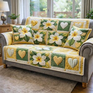 May include: A grey sofa adorned with a patchwork quilt and matching cushions. The quilt features large white flowers, green leaves, and yellow hearts. The cushions echo the floral design. The room is bright, with a view of the outdoors.