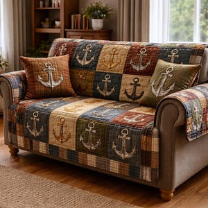 May include: A sofa with a patchwork quilt and two matching throw pillows. The quilt and pillows feature embroidered anchors in various colors, including brown, blue, and green. The sofa has a neutral gray color and is placed in a room with wooden furniture.