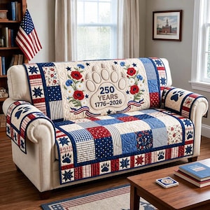 Può includere: Una fodera per divano con un tema patriottico in rosso, bianco e blu. La fodera presenta un motivo patchwork. Il pannello centrale ha un design ricamato con impronta di zampa con il testo "250 YEARS 1776-2026".