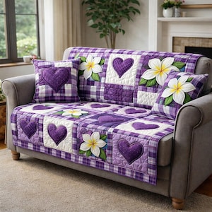 Puede incluir: Una funda de sofá a cuadros morados y blancos y cojines a juego. La funda presenta cuadrados acolchados con corazones morados y flores blancas. El sofá es gris, con una ventana y una chimenea en el fondo.