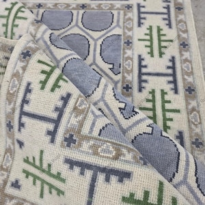 Alfombra moderna de lana anudada a mano con estampado tribal geométrico en verde salvia, azul pizarra y crema.