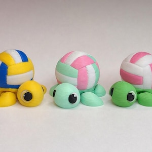 May include: Three whimsical turtle figurines, each with a volleyball-shaped shell. The turtles are yellow, mint green, and green, with volleyballs in yellow/blue, pink/mint, and pink/white. The turtles have large, expressive eyes.