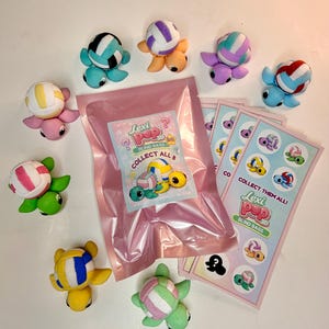 May include: A collection of colorful turtle figurines with volleyball-like shells, along with blind bags and collectible cards. The text on the packaging reads "Lexi Pop 3D Blind Bags" and "Collect Them All!"