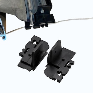 Può includere: Componenti hardware per tenda da sole in plastica nera. L'immagine mostra due diversi tipi di parti in plastica nera, tra cui staffe e connettori, progettati per l'installazione e la riparazione di tende da sole. Le parti sono mostrate su sfondo bianco.
