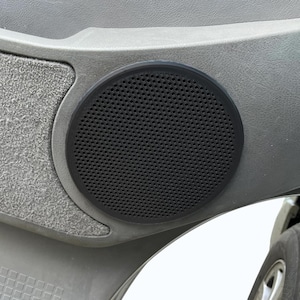 Könnte beinhalten: Ein schwarzer Lautsprecher mit einem kreisförmigen, perforierten Gitter ist in eine graue Autotürverkleidung eingesetzt. Der Lautsprecher ist von einem schwarzen Gummiring umgeben. Die Türverkleidung hat eine strukturierte Oberfläche.