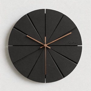 Puede incluir: Un moderno reloj de pared negro con un diseño único. La esfera del reloj está dividida en segmentos triangulares, con manecillas de color cobre y la palabra "Goodtime" impresa. El reloj tiene un diámetro de aproximadamente 30 cm.