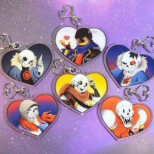 May include: A selection of heart-shaped keyrings showcasing cartoon characters. Each keyring displays a unique character design in colours such as blue, red, yellow, and black. The keyrings are fitted with silver-coloured metal clasps.