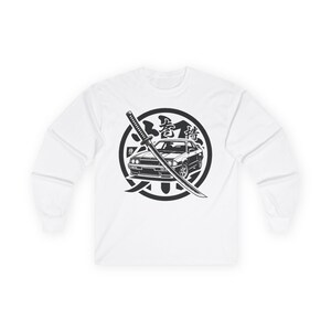 May include: White long-sleeve shirt featuring a black and white graphic. The graphic includes a car, a katana sword, and Japanese text within a circular design. The shirt is made of a soft, comfortable material.