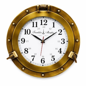 Può includere: Un orologio da parete rotondo color ottone con quadrante bianco. L'orologio ha numeri e lancette nere, con una lancetta dei secondi rossa. Il quadrante recita "Franklin & Murphy EST 868". Il design ricorda un oblò di una nave.