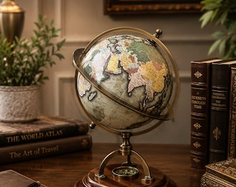 May include: A decorative globe featuring a muted color palette of greens, yellows, and pinks, mounted on a brass-toned metal meridian ring and a circular dark wood base. The base includes an integrated compass, and the globe displays world geography.