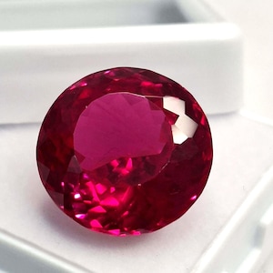 May include: A large, round, faceted ruby gemstone. The gem is a deep, saturated red color with brilliant internal reflections. The ruby is set against a white background, highlighting its color and clarity. This gemstone is suitable for jewelry.