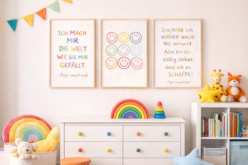 May include: Three framed art prints with colourful text and smiley faces hang on a white wall. The prints feature inspirational quotes in German. A white dresser with colourful knobs and a rainbow decor are in front of the wall.
