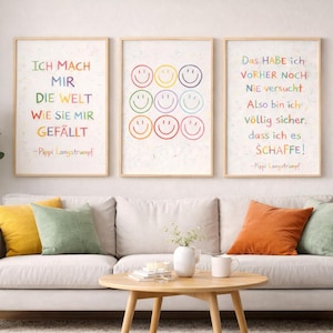 May include: Three framed art prints with German text and smiley faces in rainbow colours. The prints are displayed above a white sofa with colourful cushions. A round wooden coffee table and a potted plant complete the room's decor.