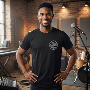 Può includere: Una maglietta nera con un logo circolare bianco che recita "KARIS Worship Generation". L'immagine mostra una persona sorridente in uno studio di registrazione, con un microfono, batteria e tastiera sullo sfondo.