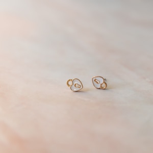 May include: A pair of gold heart-shaped earrings with a keyhole design. The earrings are white with gold accents.