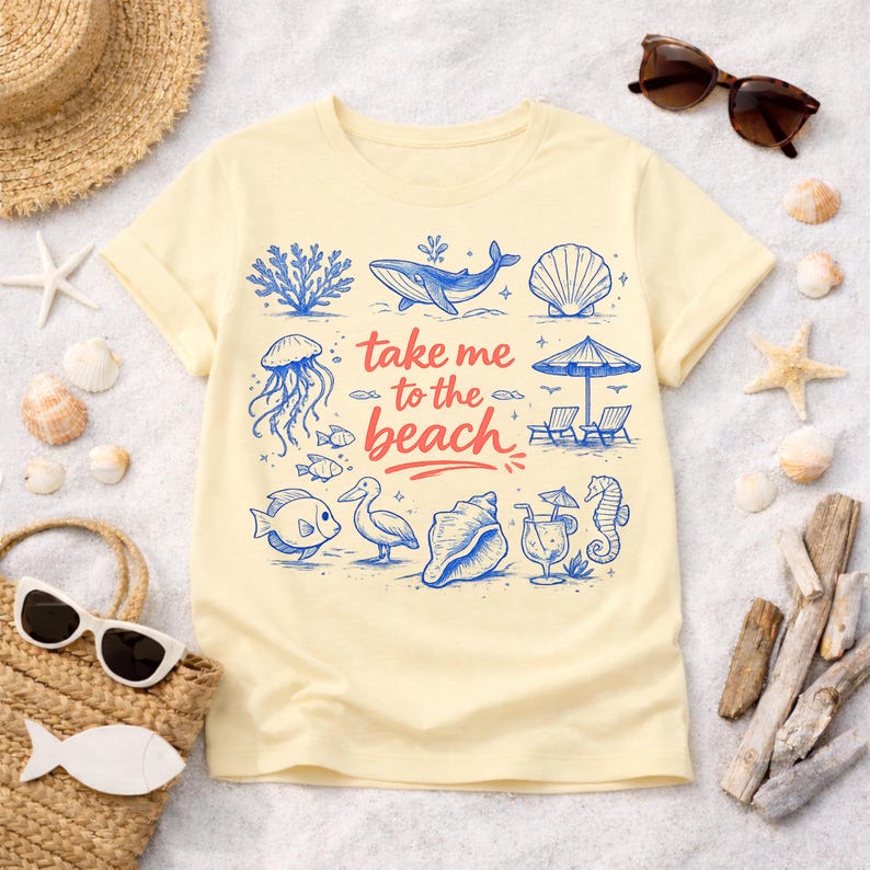 K&ouml;nnte beinhalten: Ein hellgelbes T-Shirt mit einem Strandmotiv. Das Design umfasst blaue Illustrationen von Meereslebewesen und den Satz "take me to the beach" in Rot und Blau. Das T-Shirt ist von Strandaccessoires umgeben.