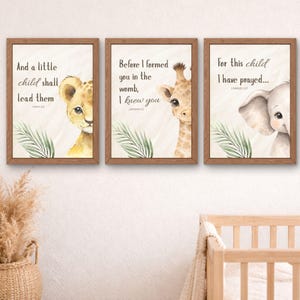 Può includere: Tre stampe artistiche incorniciate con illustrazioni ad acquerello di un cucciolo di leone, una giraffa e un elefante. Ogni stampa presenta un versetto biblico e foglie tropicali. Le cornici sono di colore marrone caldo e lo sfondo è beige chiaro.