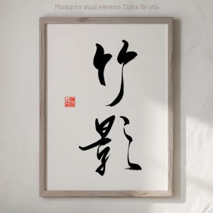 Könnte beinhalten: Gerahmtes Kunstwerk mit japanischer Kalligraphie in schwarzer Tinte auf weißem Hintergrund. Die Kalligraphie umfasst zwei Schriftzeichen und einen roten Siegelstempel in der unteren linken Ecke. Der Rahmen ist hellholzfarben.