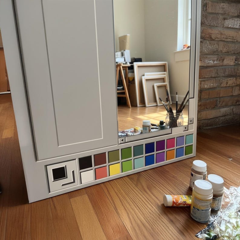 May include: A gray cabinet with a mirror and a built-in color palette. The palette features a variety of colors, including black, white, red, yellow, green, blue, and purple. Paint tubes and jars are on the floor.