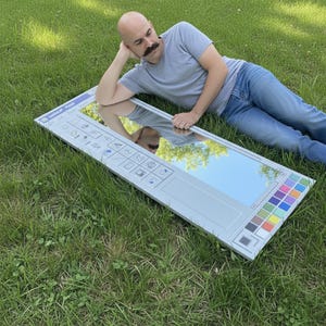 May include: A large rectangular mirror designed to resemble the Microsoft Paint interface, complete with icons, color palette, and a title bar. The mirror is lying on green grass.