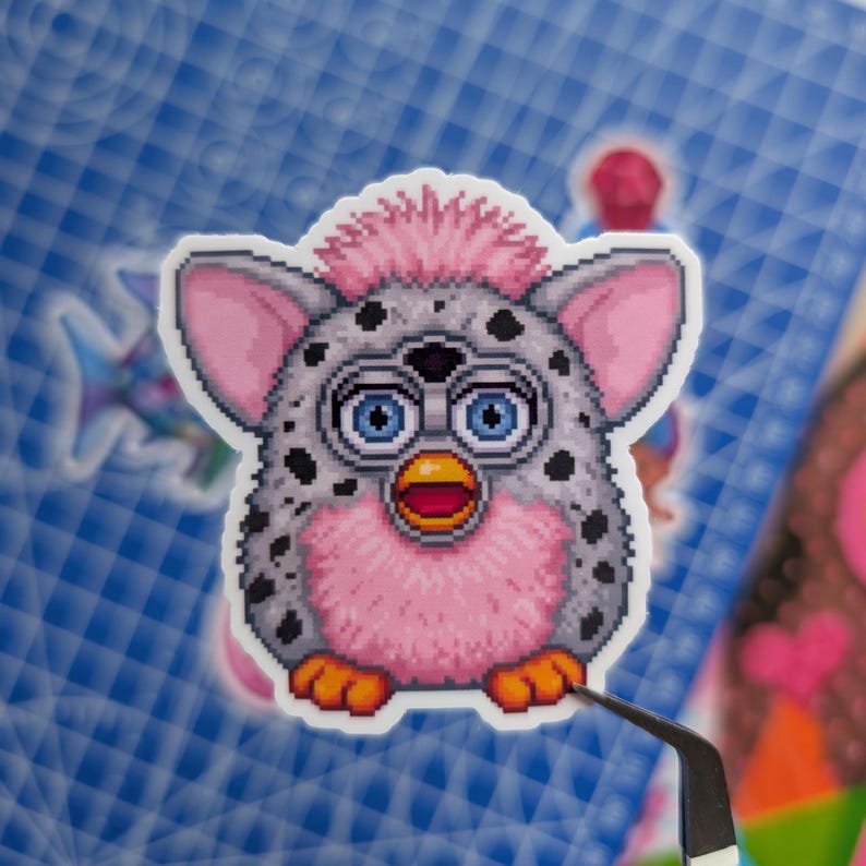 May include: A pixel art sticker of a creature with a light gray body covered in black spots, a pink tuft of hair on its head, large blue eyes, a yellow beak, and orange feet. The creature has large ears and a pink chest area.