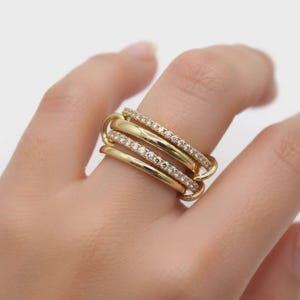 May include: A multi-band gold ring featuring four distinct bands. Two bands are smooth and polished gold, while the other two bands are encrusted with small, clear, sparkling stones set along the entire outer surface of the ring bands.